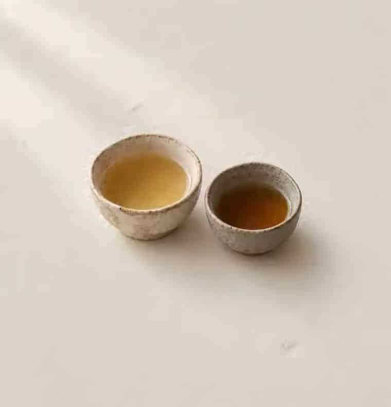 Two stoneware cups, one of pale gold tea and one of amber tea